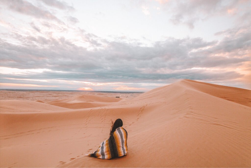 solo female travel - woman sitting in the desert, thinking