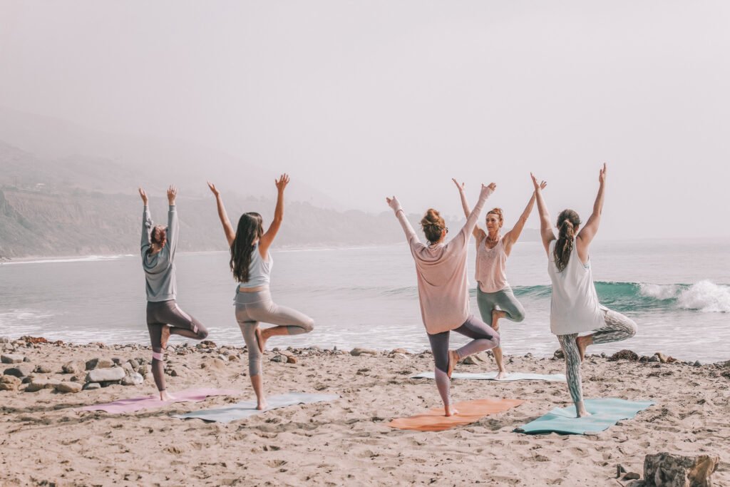 group of women doing yoga by the ocean